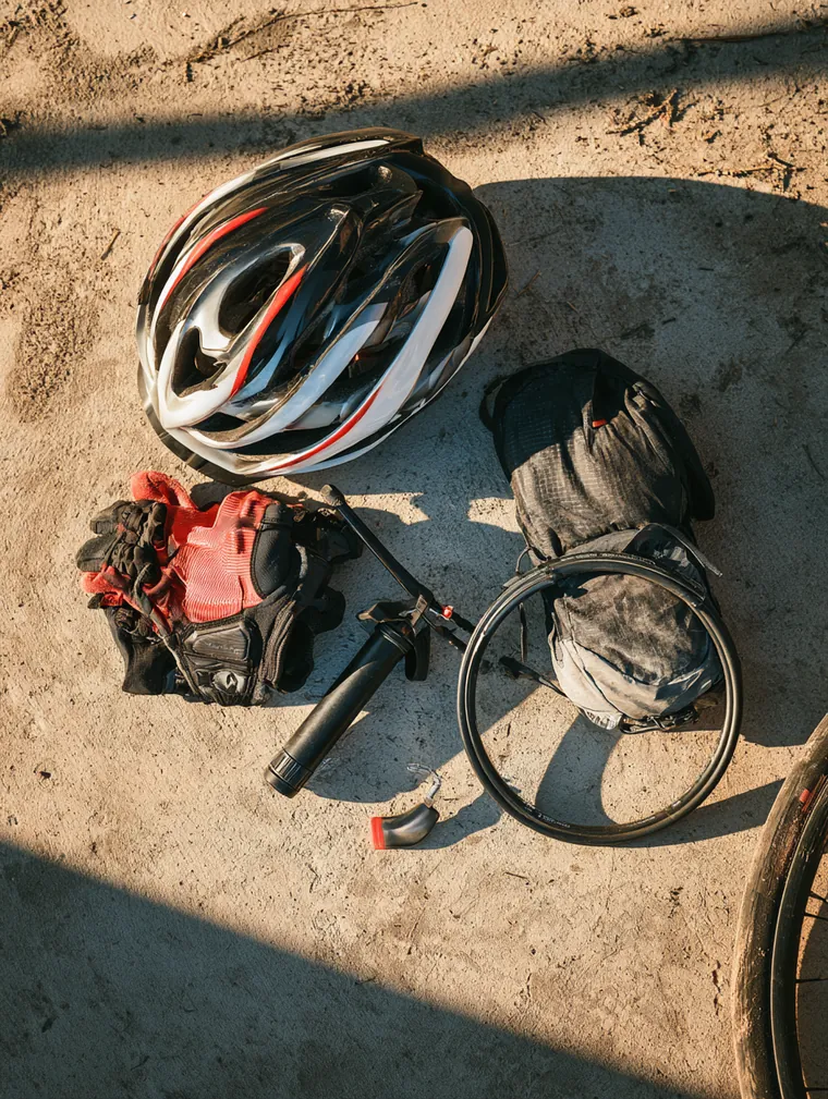Overhead flat lay of a cycling helmet, gloves, a bike pump and a spare tube laid out on a driveway